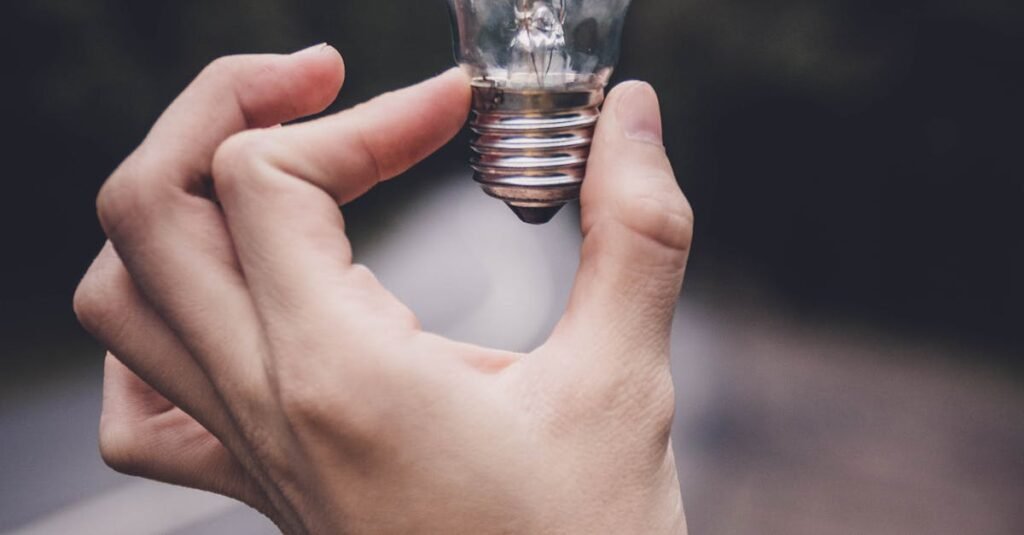 Close-up of a hand holding a lightbulb against a blurred outdoor road background.
